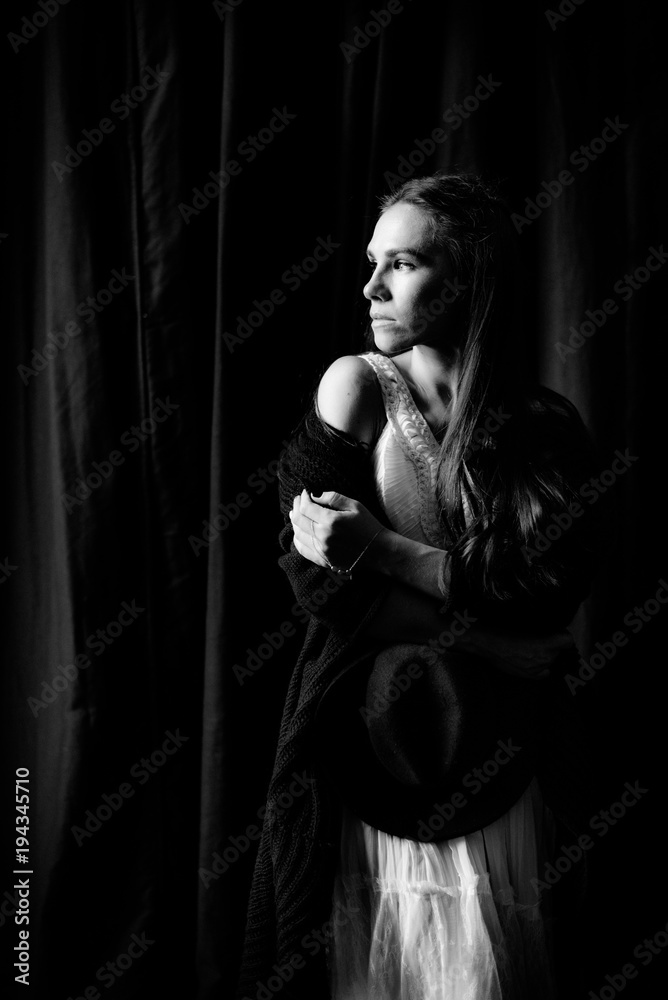 Black and white portrait of a sensual girl on a black background, which looks away, light from the window shines on her