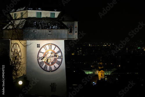 The clock tower of Graz in the foreground with the Franziskanerkirche church in the background (night scene)