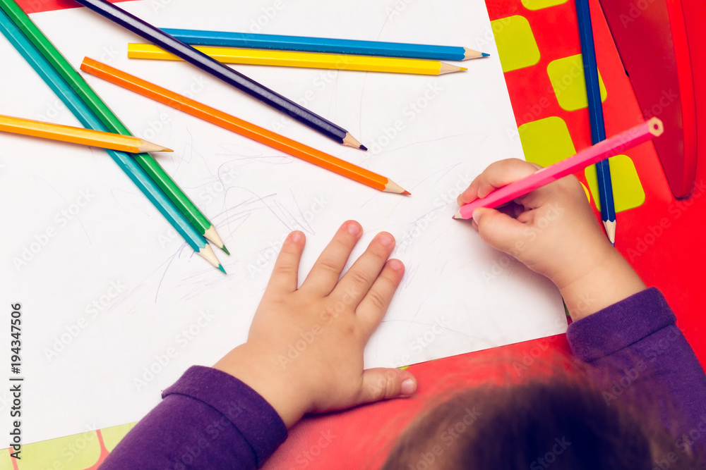 On the red table, children's hands with colored pencils and a blank sheet of paper On the red table, children's hands with colored pencils and a blank sheet of paper