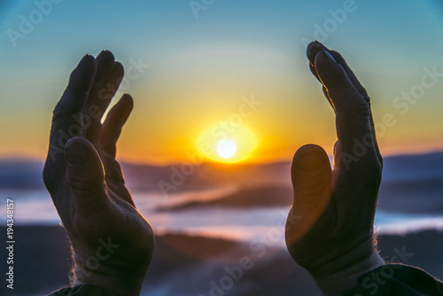 Hands of an old man reaching for the sun at sunrise, closeup. Concept of birth new life