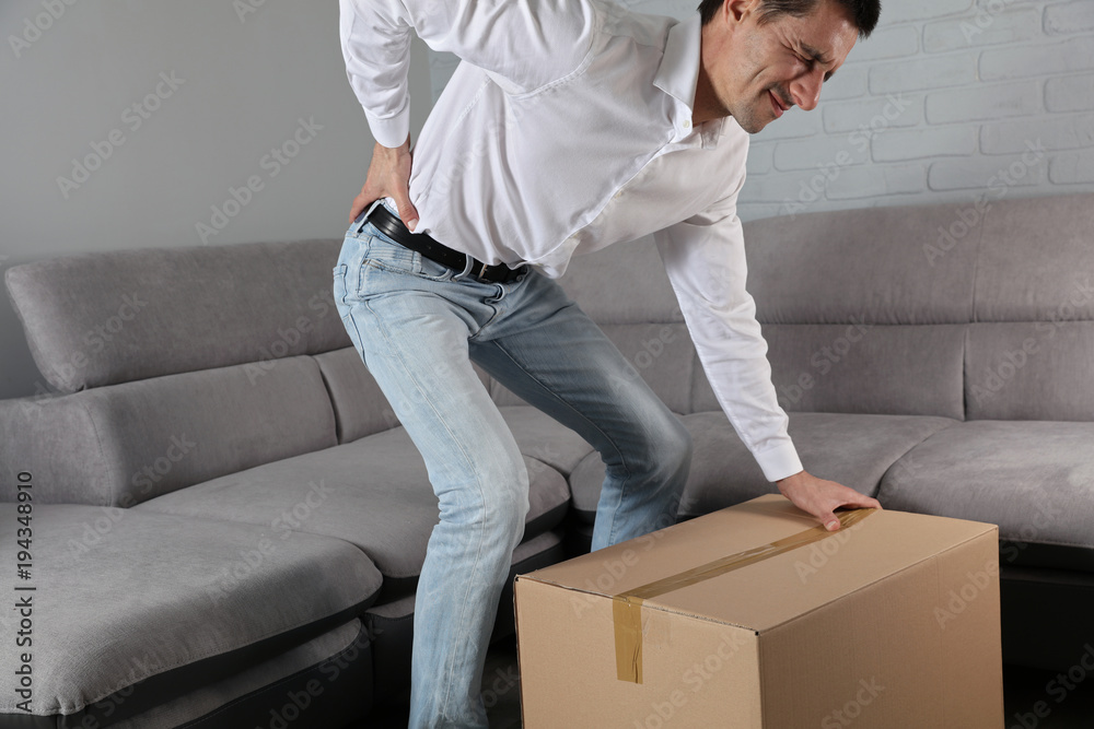 Man suffering from back pain moving boxes in his new house . Muscle
