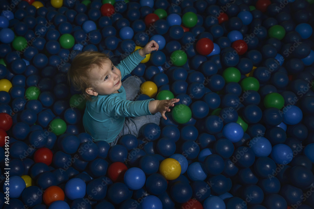 happy little child plays on a playground filled with colorful plastic balls.