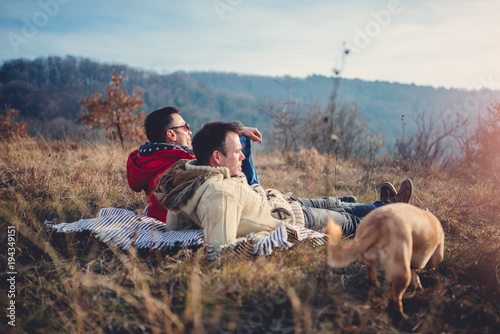 Gay male couple laying on blanket in grass with dog © kerkezz