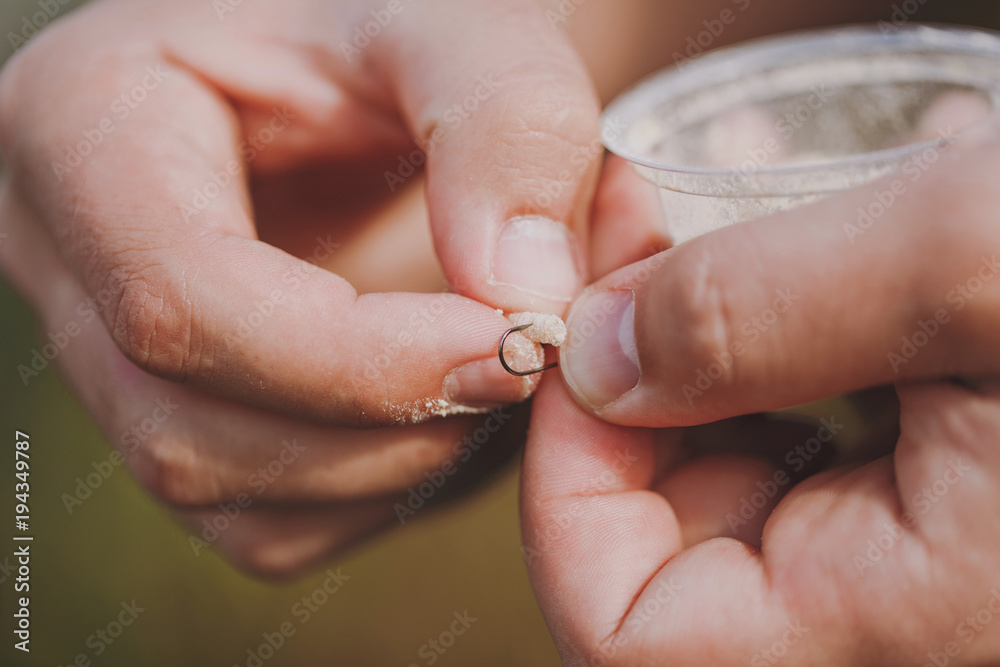 Close up Men's hands hold a small box with maggots and put bait on the hook to fish with a fishing rod on a blurry pastel brown background. Lifestyle, recreation, leisure concept. Fisherman with worm.