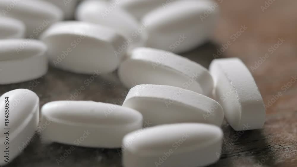 White prescription pills fall into a large pile in slow motion. The pain killer tablets represent pharmaceutical substance abuse in teens and recreational drug use of opiates. White prescription pills fall into a large pile in slow motion. The pain killer tablets represent pharmaceutical substance abuse in teens and recreational drug use of opiates.