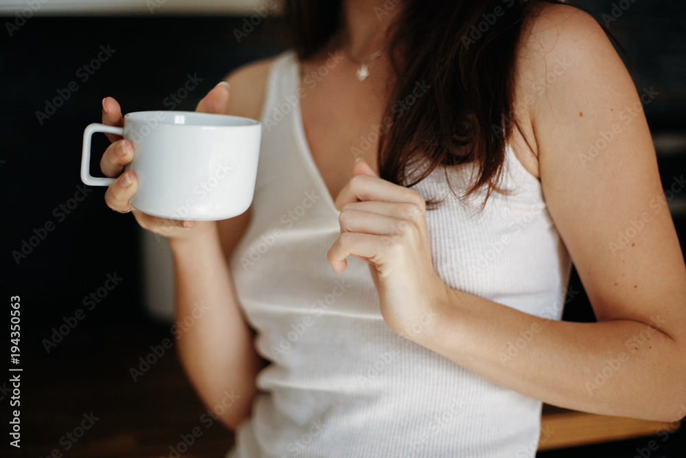 Closeup of beautiful young sexy Caucasian woman with dark red hair wearing white tshirt in kitchen drinking coffee. Natural beauty youth look. Girl in underwear at home Closeup of beautiful young sexy Caucasian woman with dark red hair wearing white tshirt in kitchen drinking coffee. Natural beauty youth look. Girl in underwear at home