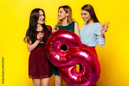 Happy Women's Day. Smiling attractive girls drinking a champagne, celebrating international holiday, March 8, holding big air balloon in form of number eight.