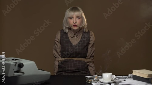 Portrait of frightened woman being kidnapped in workplace and suffering with tied hands and mouth, isolated over brown wall
