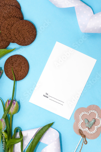 Spring tulip flowers, gift paper card on turquoise background from above in flat lay style. Greeting for Womens or Mothers Day.