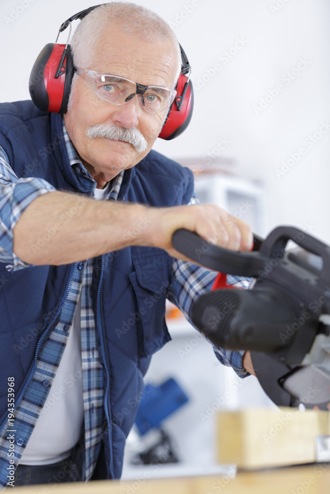 senior man wearing ear protectors while using circular saw senior man wearing ear protectors while using circular saw