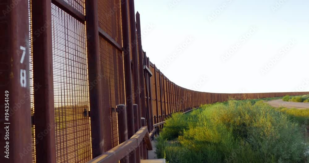 Camera tilts down to reveal the rusted metal fence separating the borderline between America and Mexico. The imposing wall prevents illegal emigration and aliens from crossing the border between the t