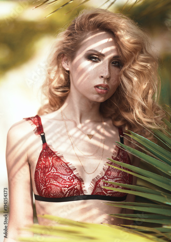 Fashion Vogue style beauty photo shoot of sexy blonde girl model in red black lace lingerie underwear: pants and bra. Sea, palms and nature at background. Close up portrait of beautiful young woman photo