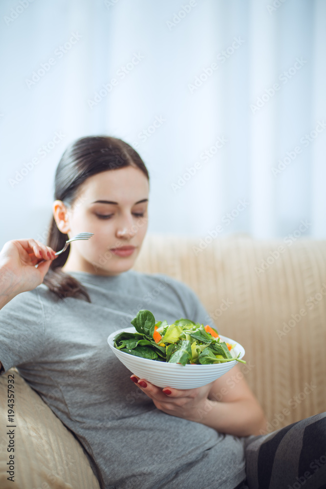Woman in sportswear with plate of vegetarian vegetable salad. Young sporty model at livingroom. Health, beauty and fitness concept. Woman in sportswear with plate of vegetarian vegetable salad. Young sporty model at livingroom. Health, beauty and fitness concept.