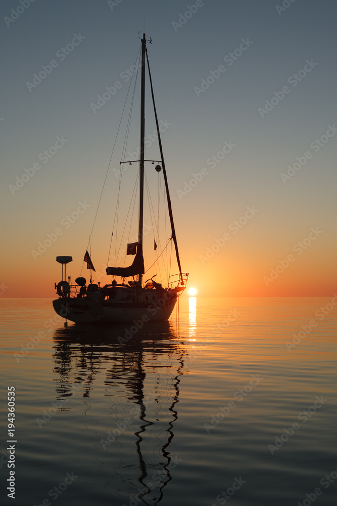 A silhouette of a sailboat right at sunset at a calm anchorage in the Exumas Island chain in the Bahamas.