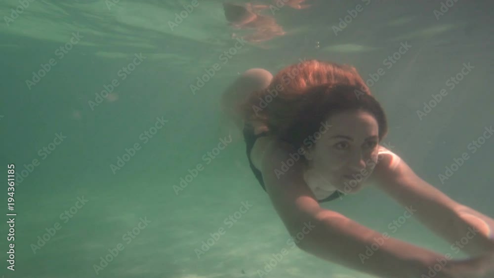 Woman in blue bathing suit swimming underwater in slow motion