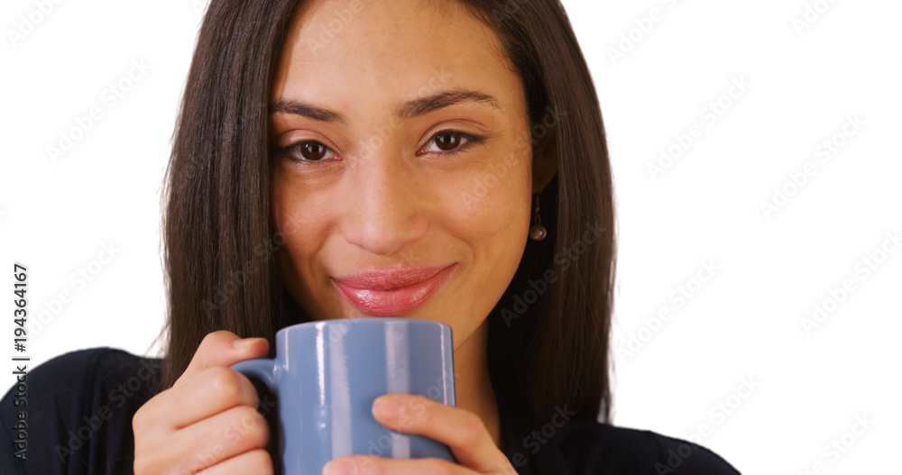 A close-up portrait of a Hispanic woman drinking coffee on a white background. A Latina looks at the camera on a blank backdrop A close-up portrait of a Hispanic woman drinking coffee on a white background. A Latina looks at the camera on a blank backdrop