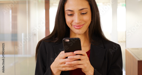 A Latina office professional texts on her mobile phone at work. A Hispanic office worker uses her smart phone in her office