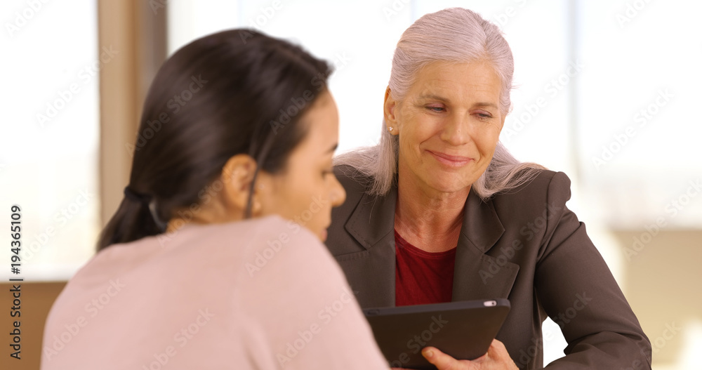 A smiling business executive has a meeting with her employee. An older office worker with a tablet meets with an employee A smiling business executive has a meeting with her employee. An older office worker with a tablet meets with an employee