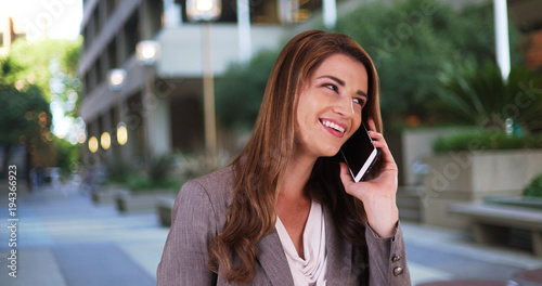 Attractive businesswoman talking on smartphone at work. Woman in 20s talking on cellphone outside of work during her lunch break © rocketclips