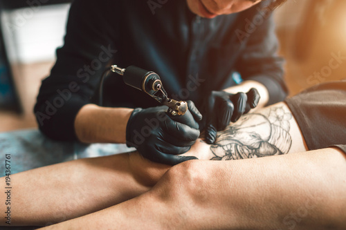 Tattoo artist in black gloves making a tattoo on the foot girls. Sterile.