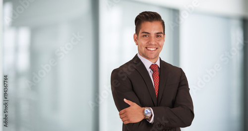 Happy smiling young Hispanic businessman standing in office with arms crossed looking at camera. Copyspace or copy space next to business professional with smile on his face photo