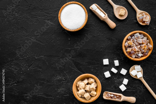 Brown and white sugar in bowls, scoop and spoon. Cane, refind, granulated, cubes, candy. Black background top view copy space photo