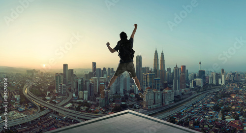 Young man jumping on rooftop with great cityscape sunrise view. photo