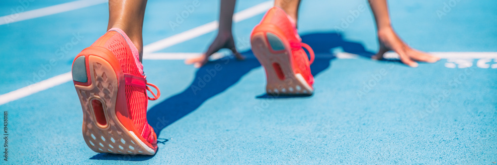 Sprinter waiting for start of race on running tracks at outdoor stadium. Sport and fitness runner woman athlete on blue run track with orange running shoes. Panorama banner.