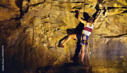 Male mountain climber reaches upwards while climbing rocky cliff face.