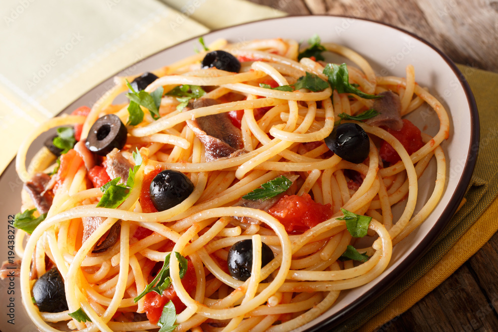 Italian food: spaghetti alla putanesca with anchovies, tomatoes, garlic, black olives and greens close-up. horizontal