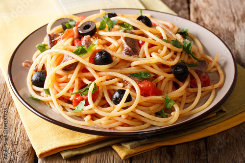 Delicious spaghetti alla putanesca with anchovies with vegetables and greens close-up. horizontal photo