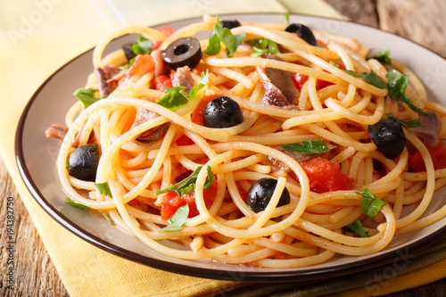 Spaghetti alla putanesca with anchovies, tomatoes, garlic and black olives close-up. horizontal