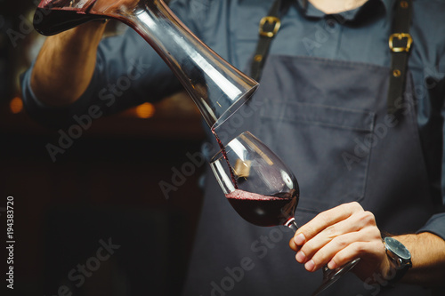 Sommelier pouring wine into glass from mixing bowl. Male waiter photo