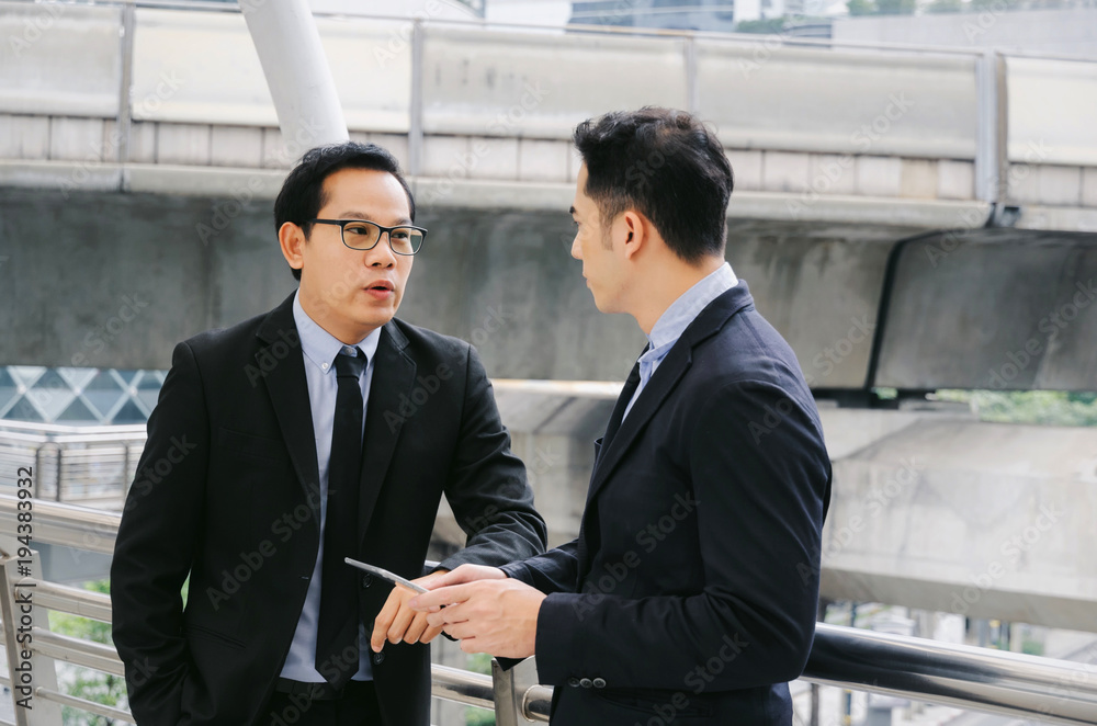 two business asian smart man in suit talking and reading information about finance news in mobile tablet together standing in modern city, network technology, internet, successful, teamwork concept two business asian smart man in suit talking and reading information about finance news in mobile tablet together standing in modern city, network technology, internet, successful, teamwork concept
