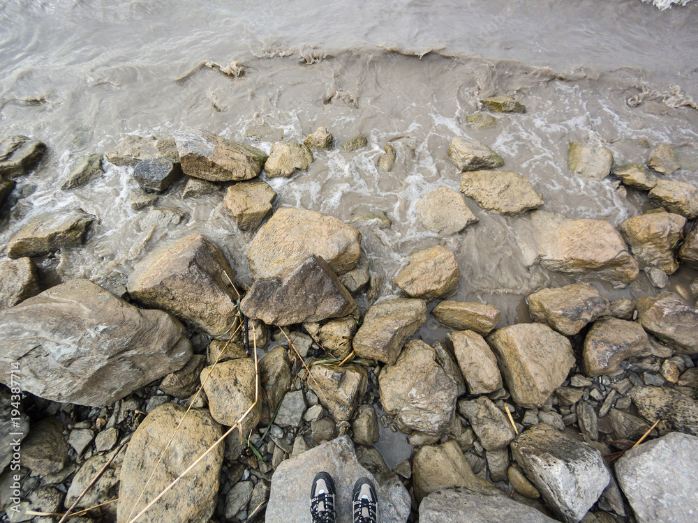 Legs in sneakers on stones in murky muddy brown shallow water of lake surf Legs in sneakers on stones in murky muddy brown shallow water of lake surf