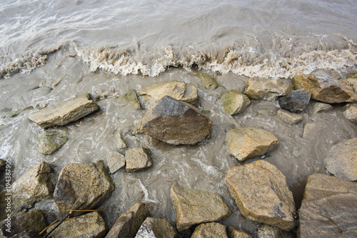 Stones in the murky muddy brown shallow water of the lake surf