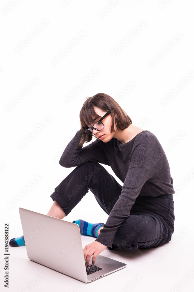 Pretty young teen girl sitting on the floor with crossed legs and using laptop isolated over white background Pretty young teen girl sitting on the floor with crossed legs and using laptop isolated over white background