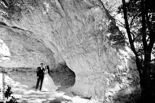 Wedding couple against cave at summer day.