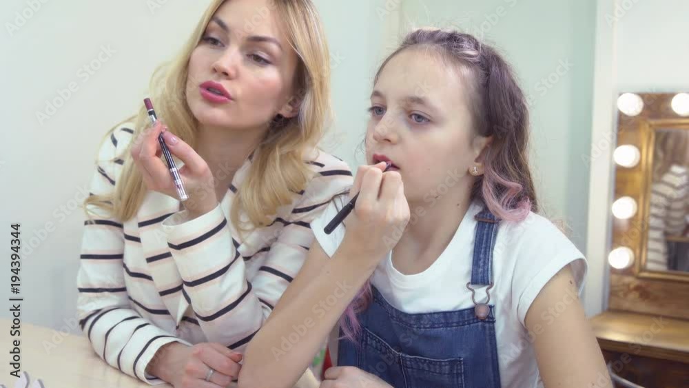 Mother and daughter in the mirror paint their lips. Reflection. Mother and daughter in the mirror paint their lips. Reflection.