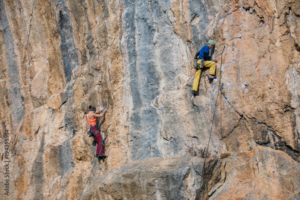Man and woman parallel climb a yellow rock with a rope, lead, side view Man and woman parallel climb a yellow rock with a rope, lead, side view