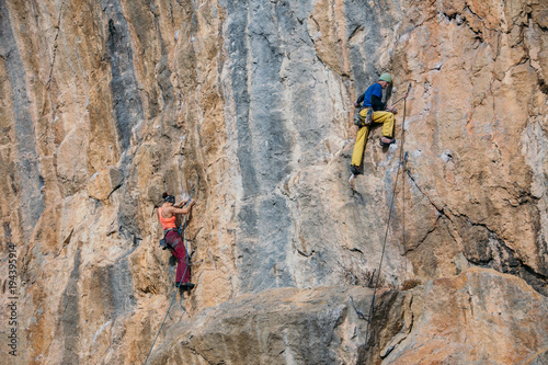 Man and woman parallel climb a yellow rock with a rope, lead, side view