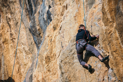 Man climbs yellow rock top rope  side view