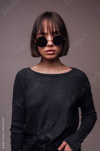 Happy young woman or teen girl in casual clothes and sunglasses isolated on gray background