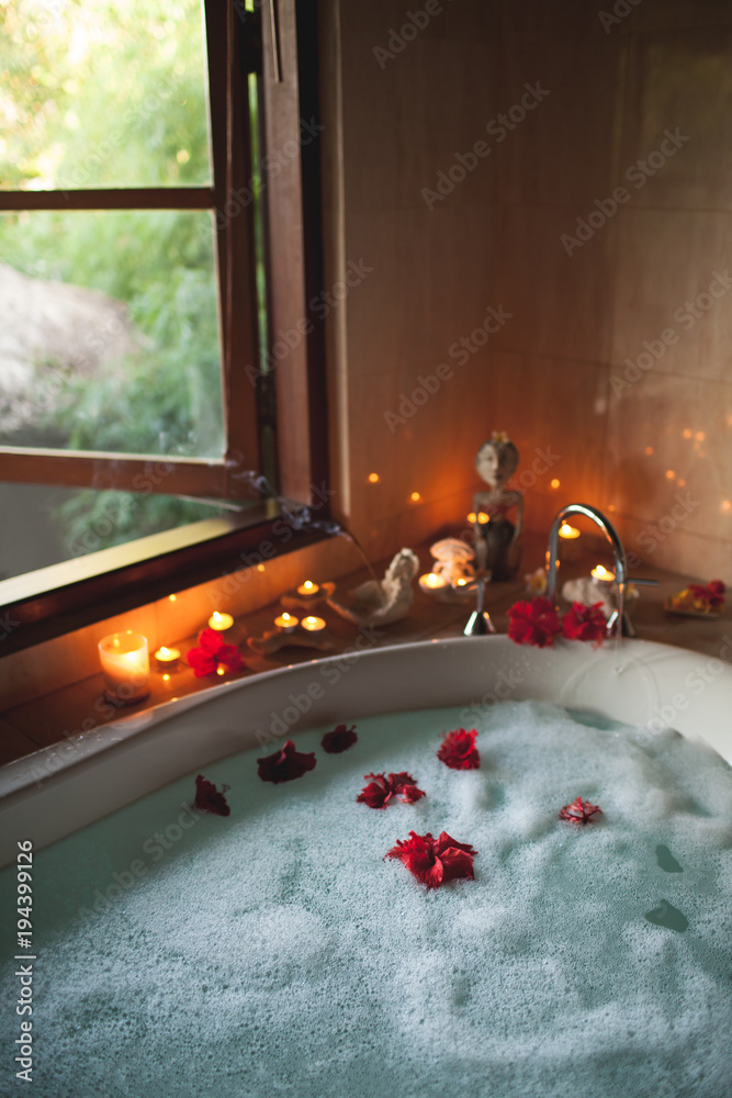 Large Filled Bath with Foam and Flowers. Romantic Atmosphere, Burning Scented Candles and Aromasticks