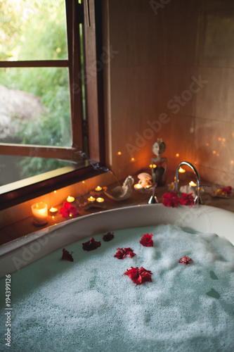 Obraz na płótnie Large Filled Bath with Foam and Flowers. Romantic Atmosphere, Burning Scented Candles and Aromasticks w salonie