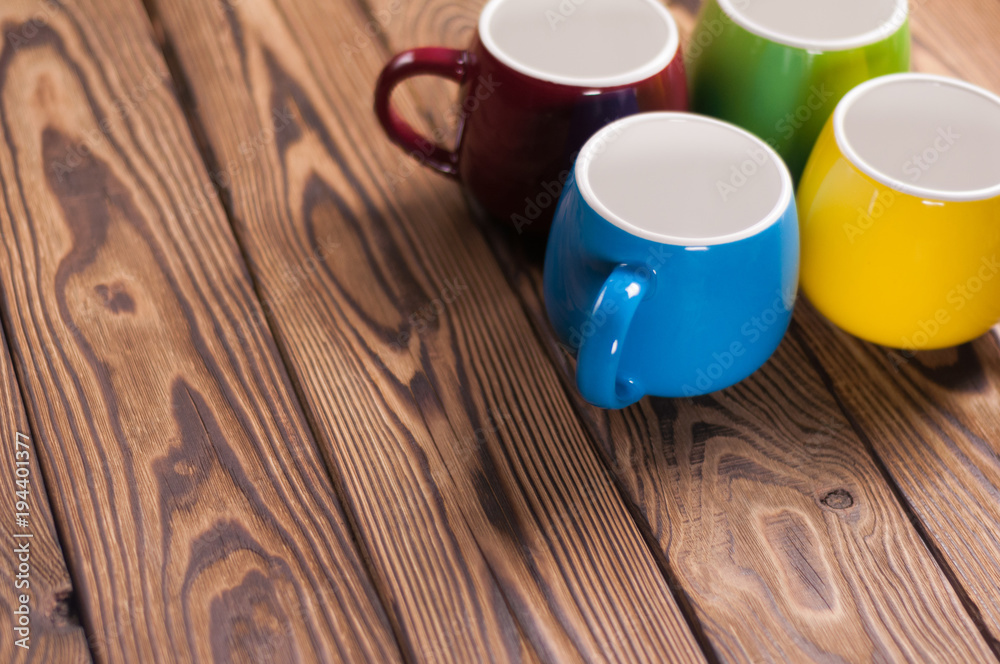 Four colored empty ceramic clean mugs on old worn brown wooden table with copy space Four colored empty ceramic clean mugs on old worn brown wooden table with copy space
