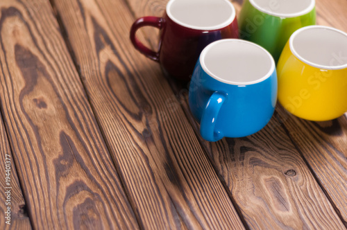 Four colored empty ceramic clean mugs on old worn brown wooden table with copy space