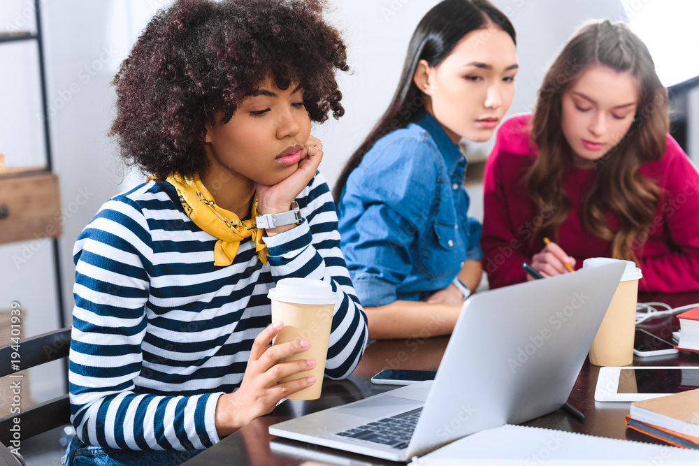 selective focus of bored african american young woman with laptop and multicultural students near by selective focus of bored african american young woman with laptop and multicultural students near by