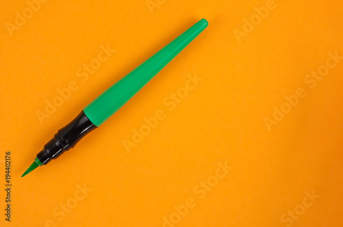 Single green color marker brush on orange background. Top view with copy space
