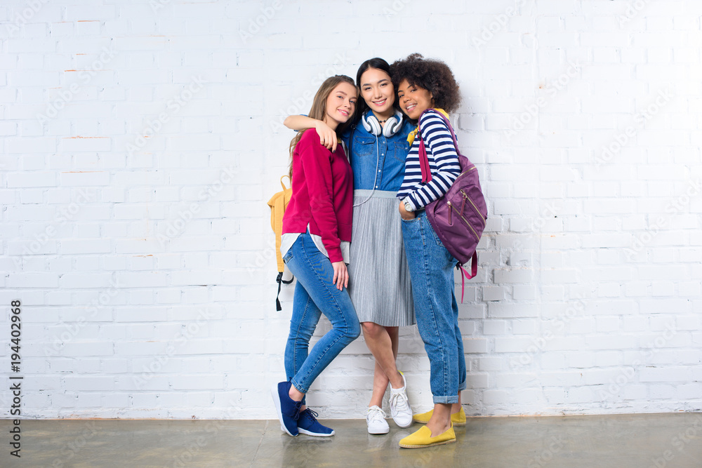 asian student hugging smiling multiethnic friends against white brick wall asian student hugging smiling multiethnic friends against white brick wall